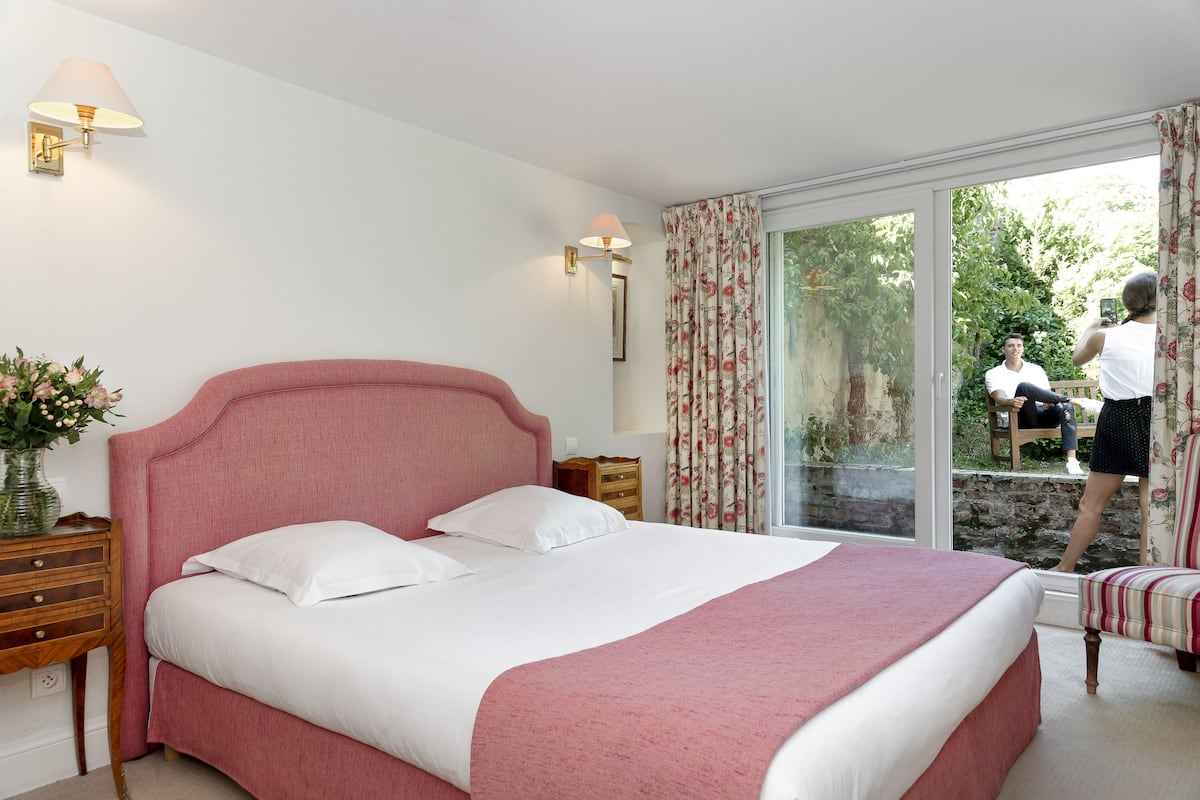 A bedroom with a large bed, a nightstand, a lamp, a dresser, and a window with curtains.