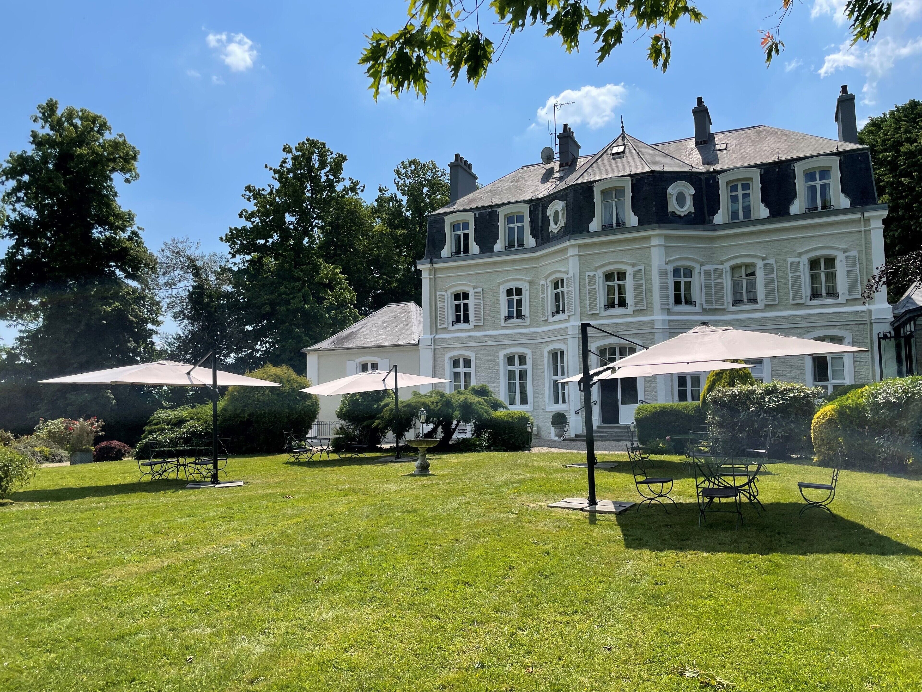 A large, historic building with multiple windows and a symmetrical facade, surrounded by a well-maintained lawn and outdoor seating areas.