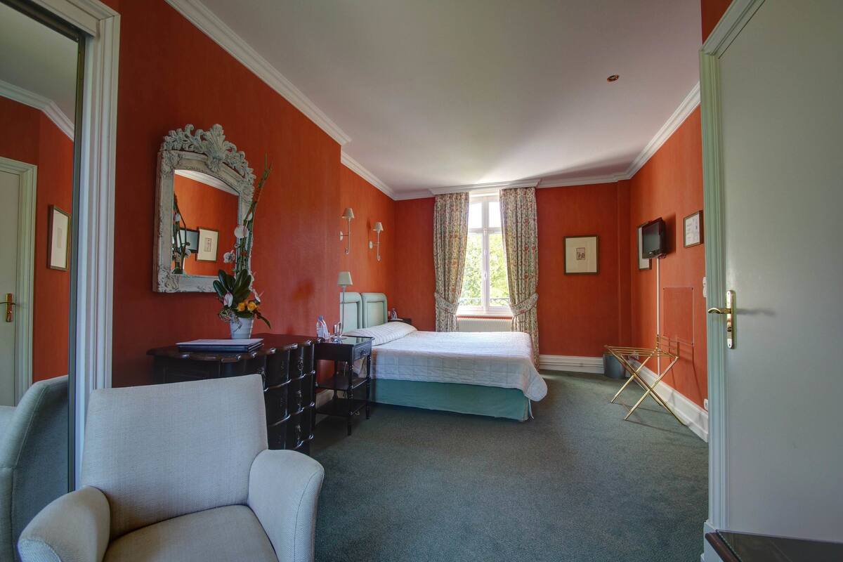 A bedroom with a bed, a dresser, a chair, a mirror, and a window with curtains.