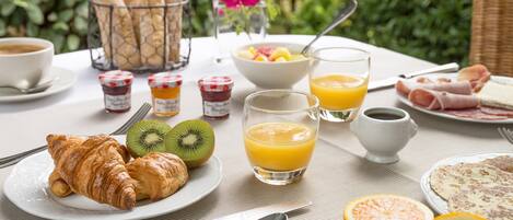 A breakfast setting with croissants, kiwi, orange juice, and a bowl of fruit.