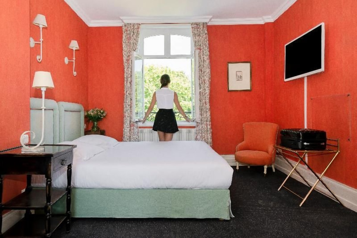 A hotel room with a bed, a desk, a chair, a TV, and a window with curtains.