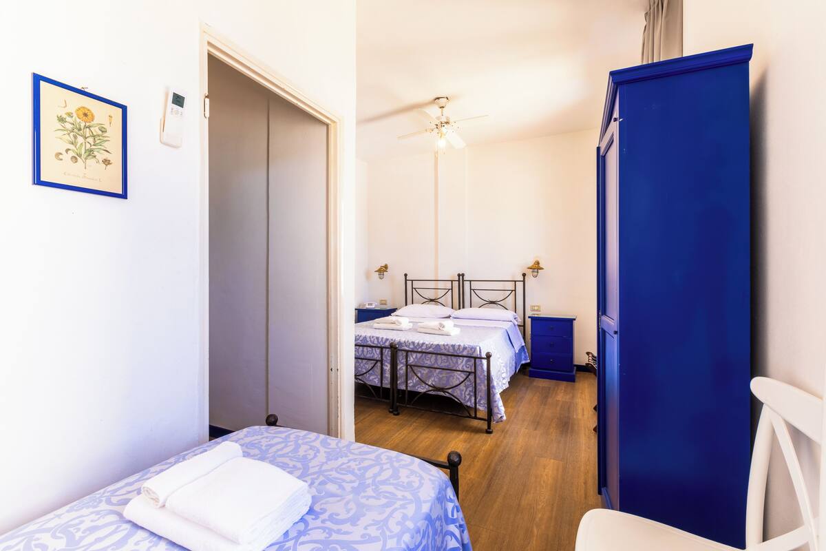Une chambre avec deux lits, un ventilateur de plafond et une armoire bleue.