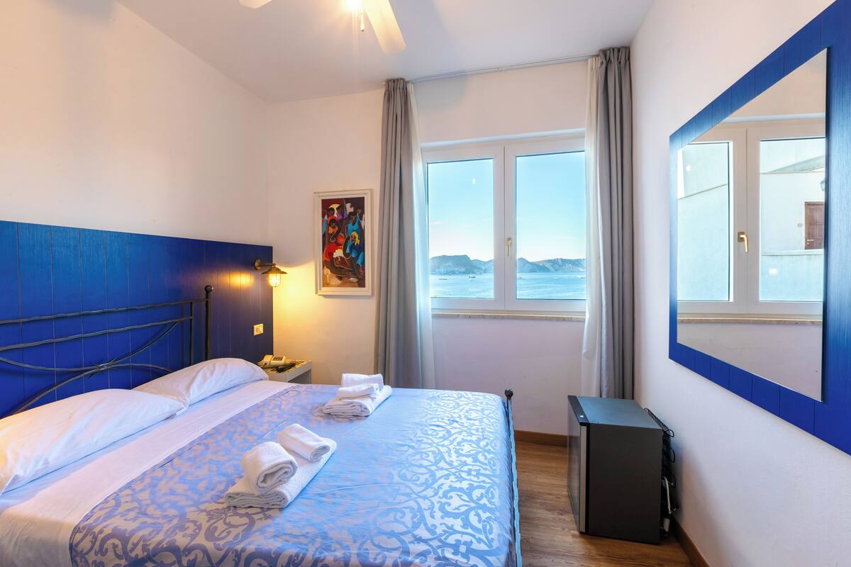 Une chambre d’hôtel avec un lit, un bureau, une fenêtre donnant sur un paysage agréable et un tableau au mur.