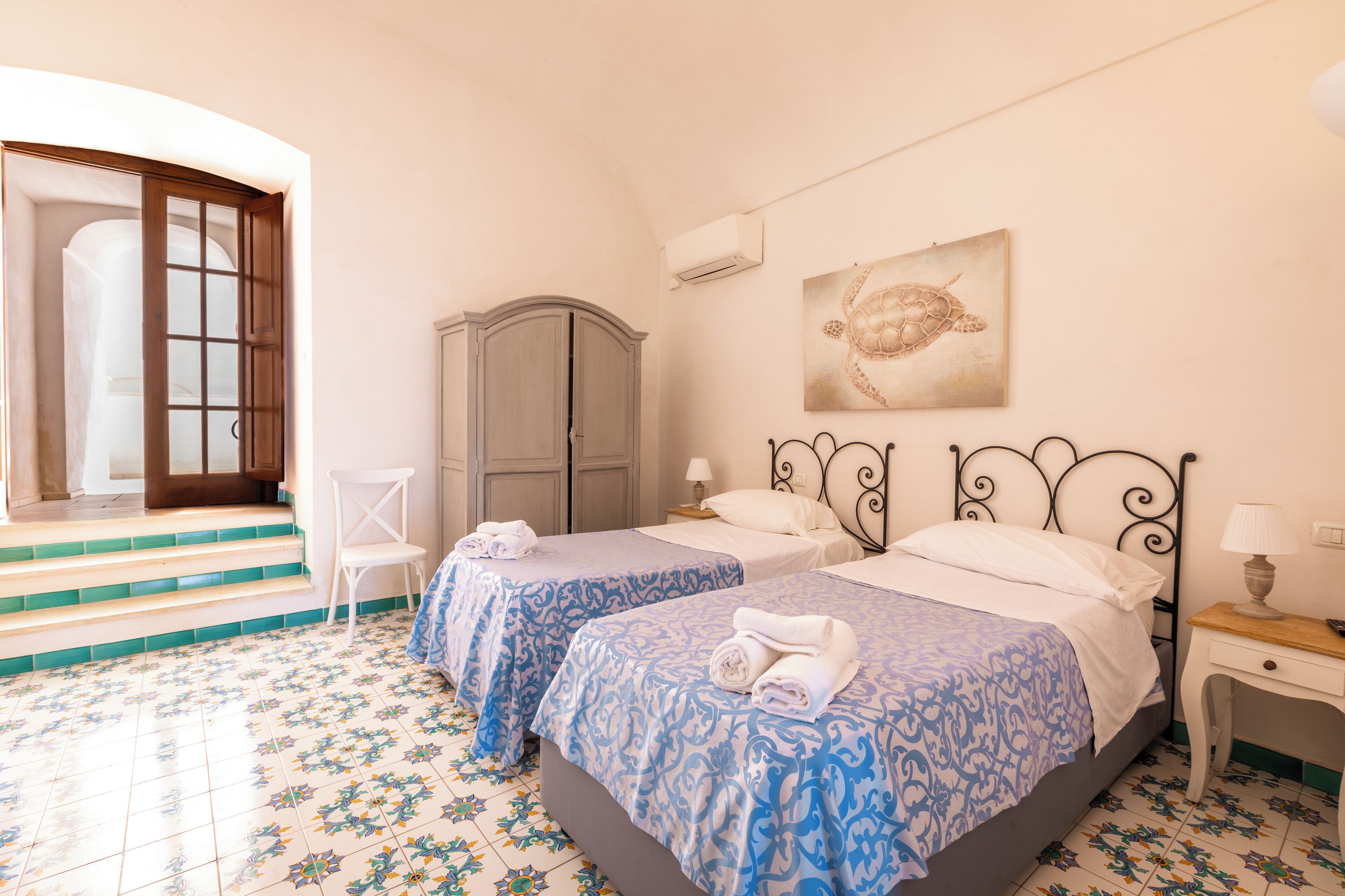 A room with two beds, a wardrobe, a chair, and a door leading to an outdoor area.