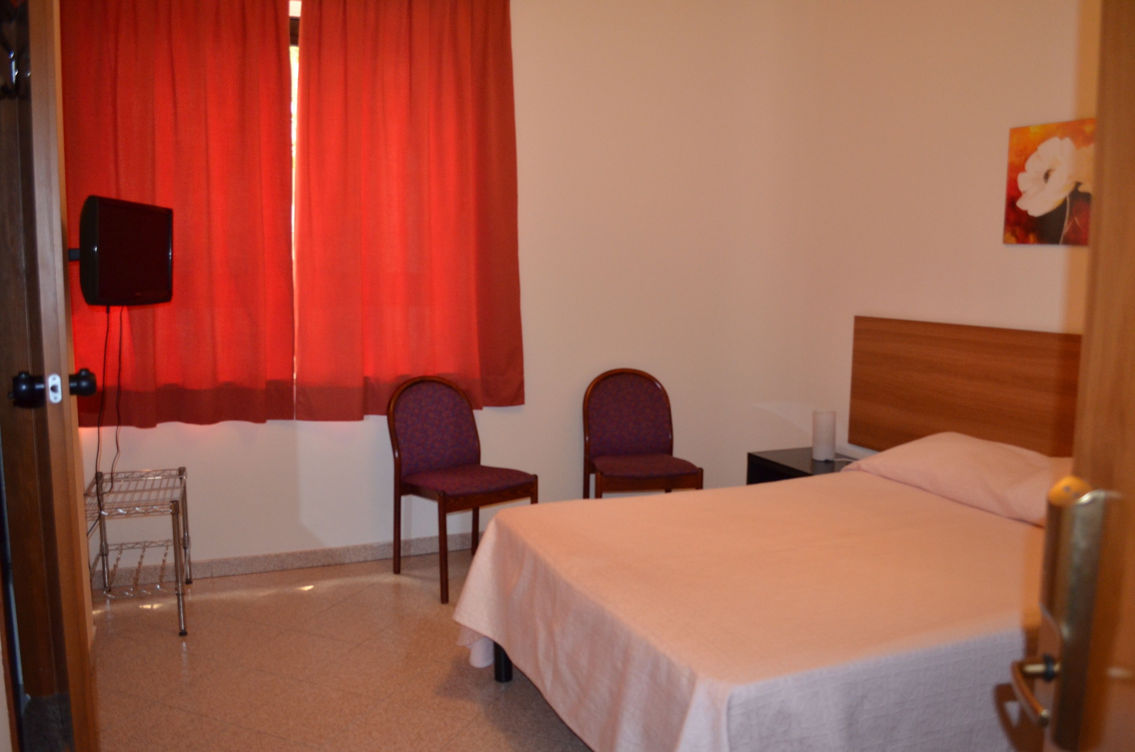 Una habitación de hotel con una cama, dos sillas, una mesita, un televisor y un cuadro en la pared.