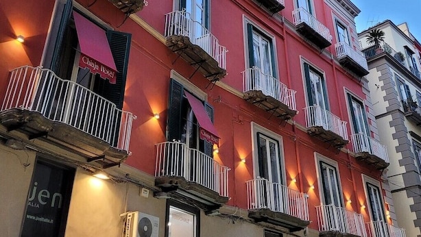 Un edificio de varios pisos con balcones, una señal visible que dice 'Chiaja Hotel' y un equipo de aire acondicionado.