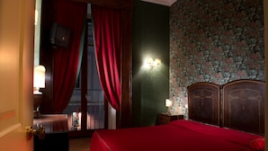 Una habitación de hotel con cama, mesita de noche, lámpara, televisor y ventana con cortinas rojas.