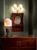 A wooden dresser with a lamp and a wall-mounted clock with two lamps.
