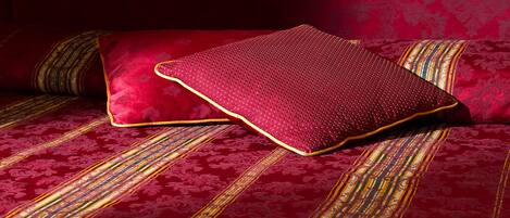A bed with a red and gold striped bedspread and a single red pillow.