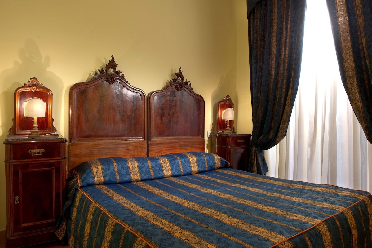 A hotel room with a large bed, two bedside tables, and a window with curtains.