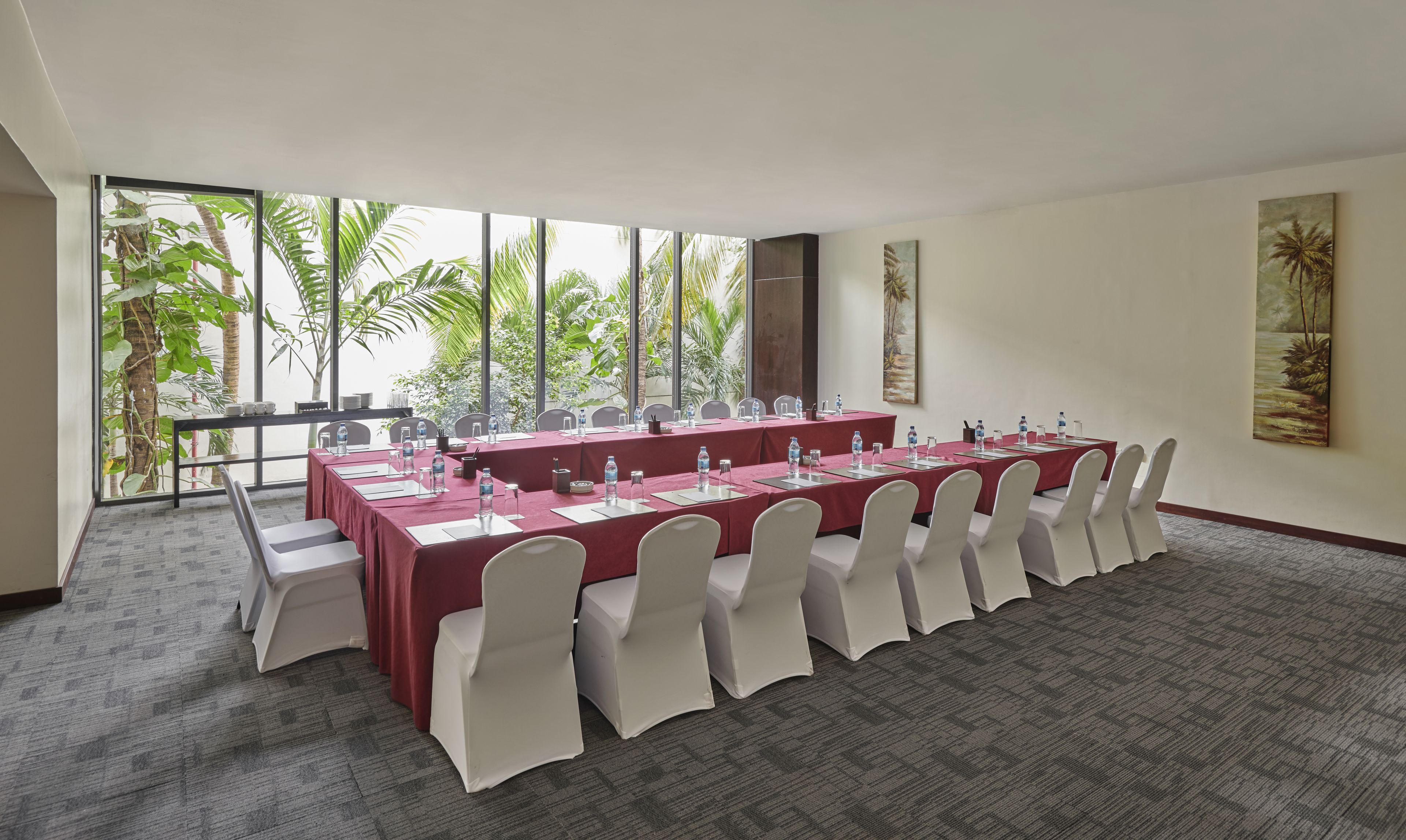 A conference room with a long table, white chairs, and a view of palm trees through large windows.