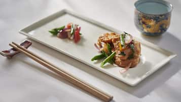 A rectangular white plate with two pieces of food, a pair of chopsticks, and a blue and yellow cup.