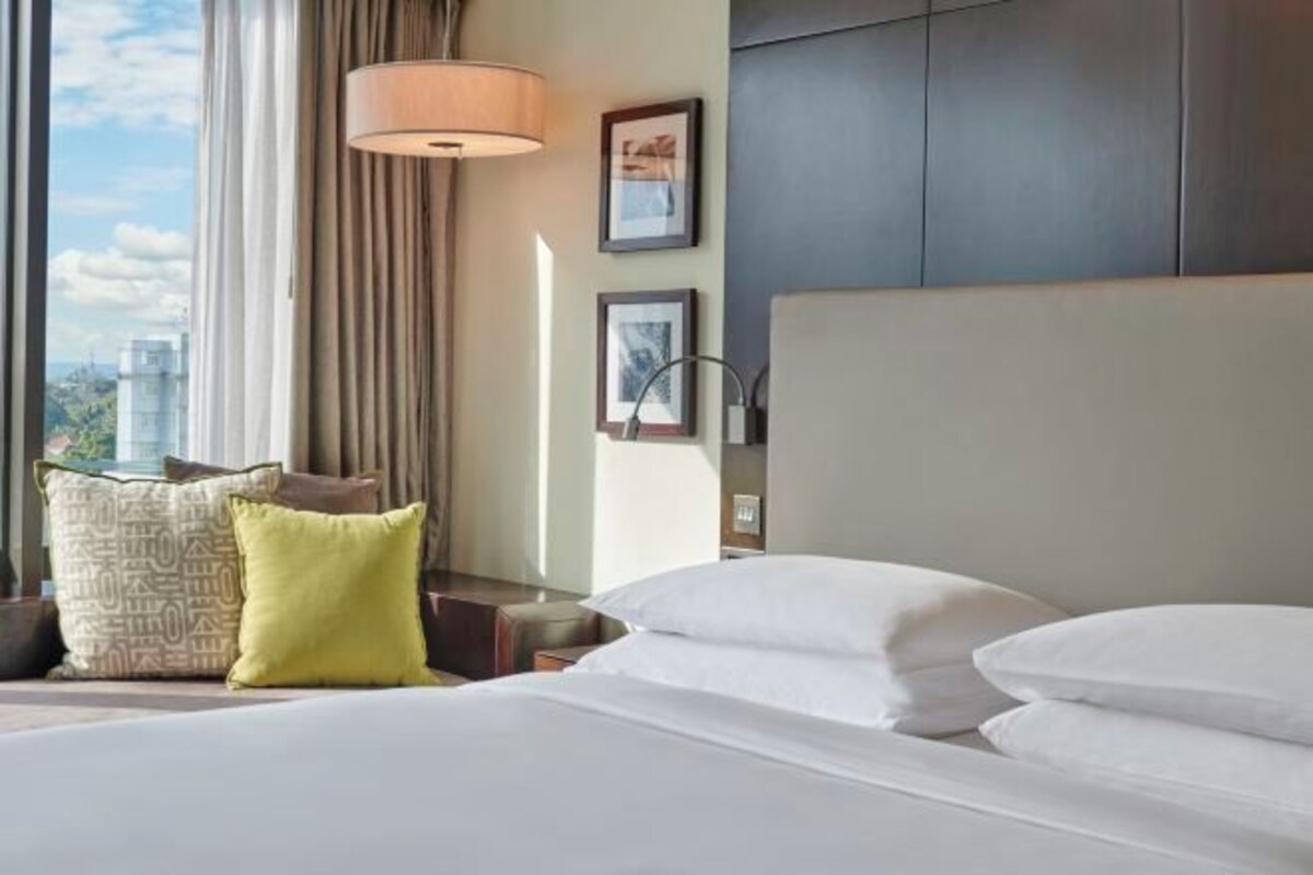 Una habitación de hotel con una cama grande, una ventana con cortinas, una lámpara de pared y cuadros enmarcados.