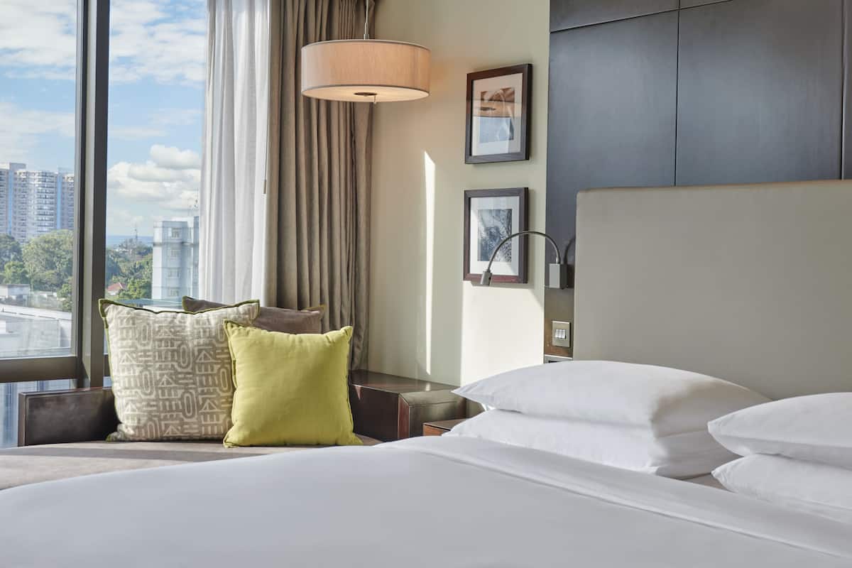 A hotel room with a large bed, a nightstand, a lamp, a window with curtains, and framed pictures on the wall.