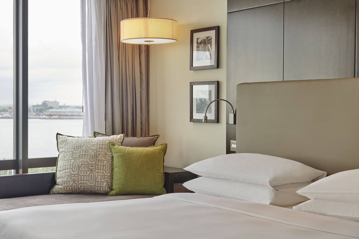 A hotel room with a large bed, a view of a body of water, and a cityscape in the background.