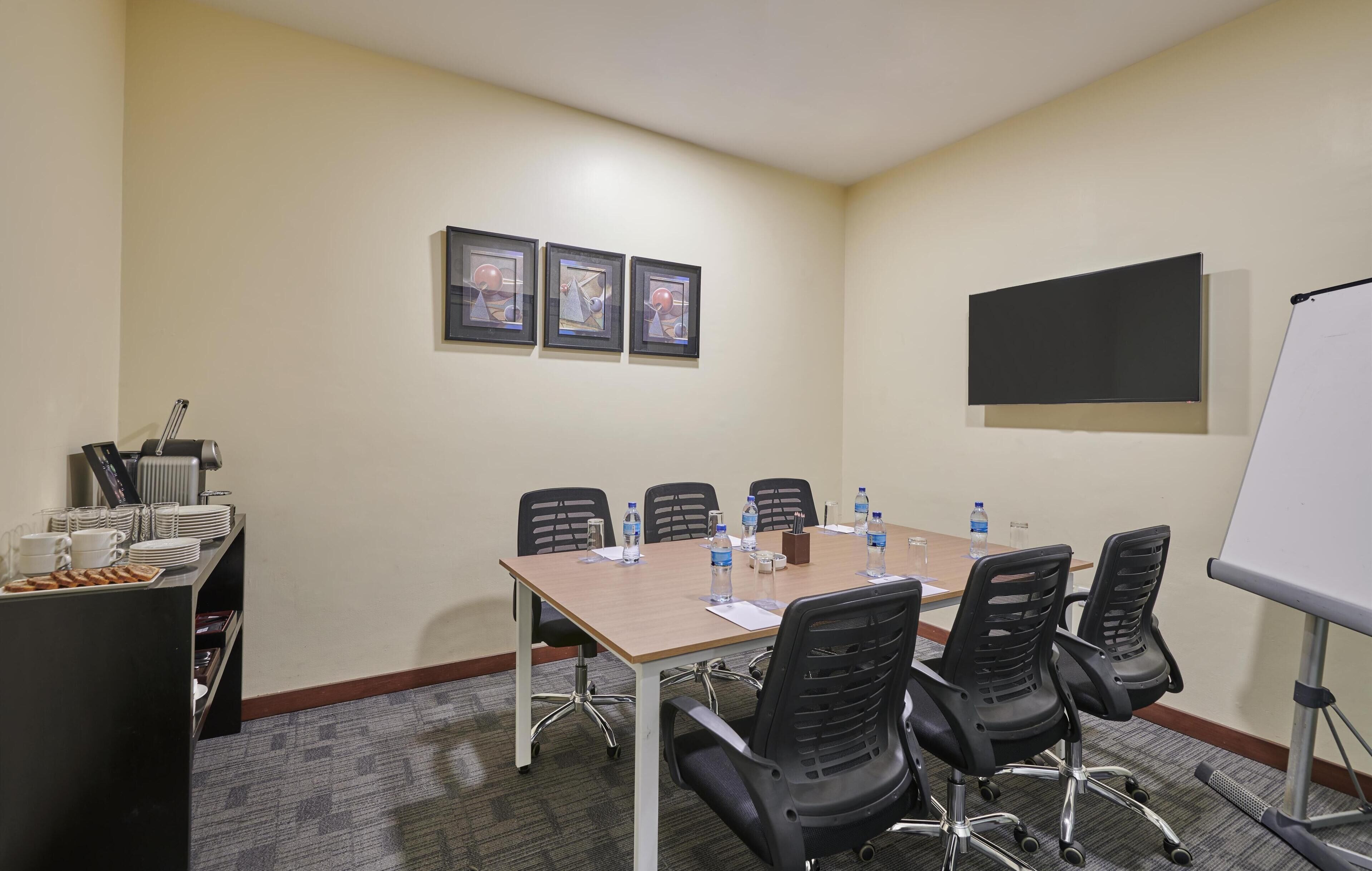 A conference room with a long table, black chairs, a whiteboard, and framed pictures on the wall.