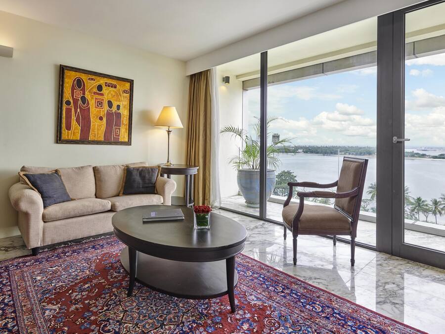 A modern hotel room with a large window offering a view of a body of water and palm trees.