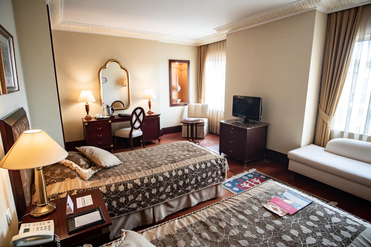 A hotel room with a bed, a sofa, a TV, a desk with a lamp, and a mirror.