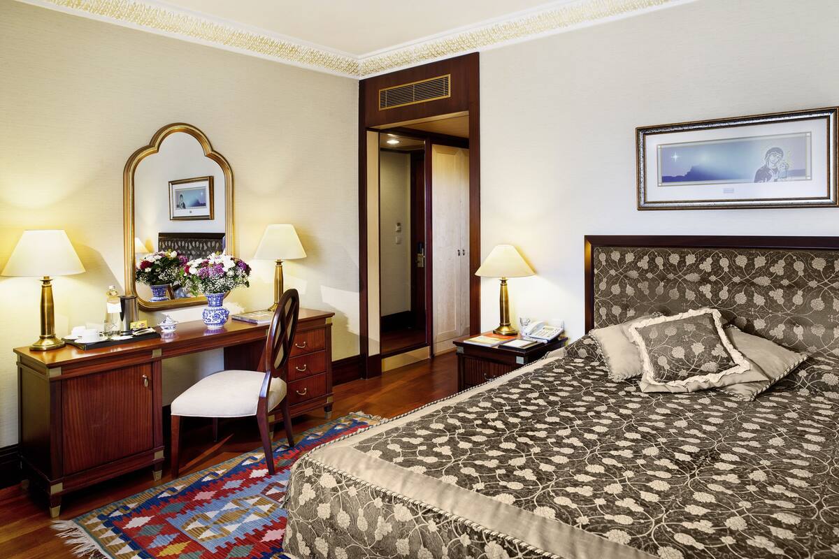 A hotel room with a bed, a desk, a chair, a mirror, and a nightstand.