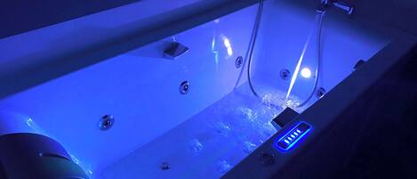 A modern bathroom with a bathtub, a handheld showerhead, and a control panel.