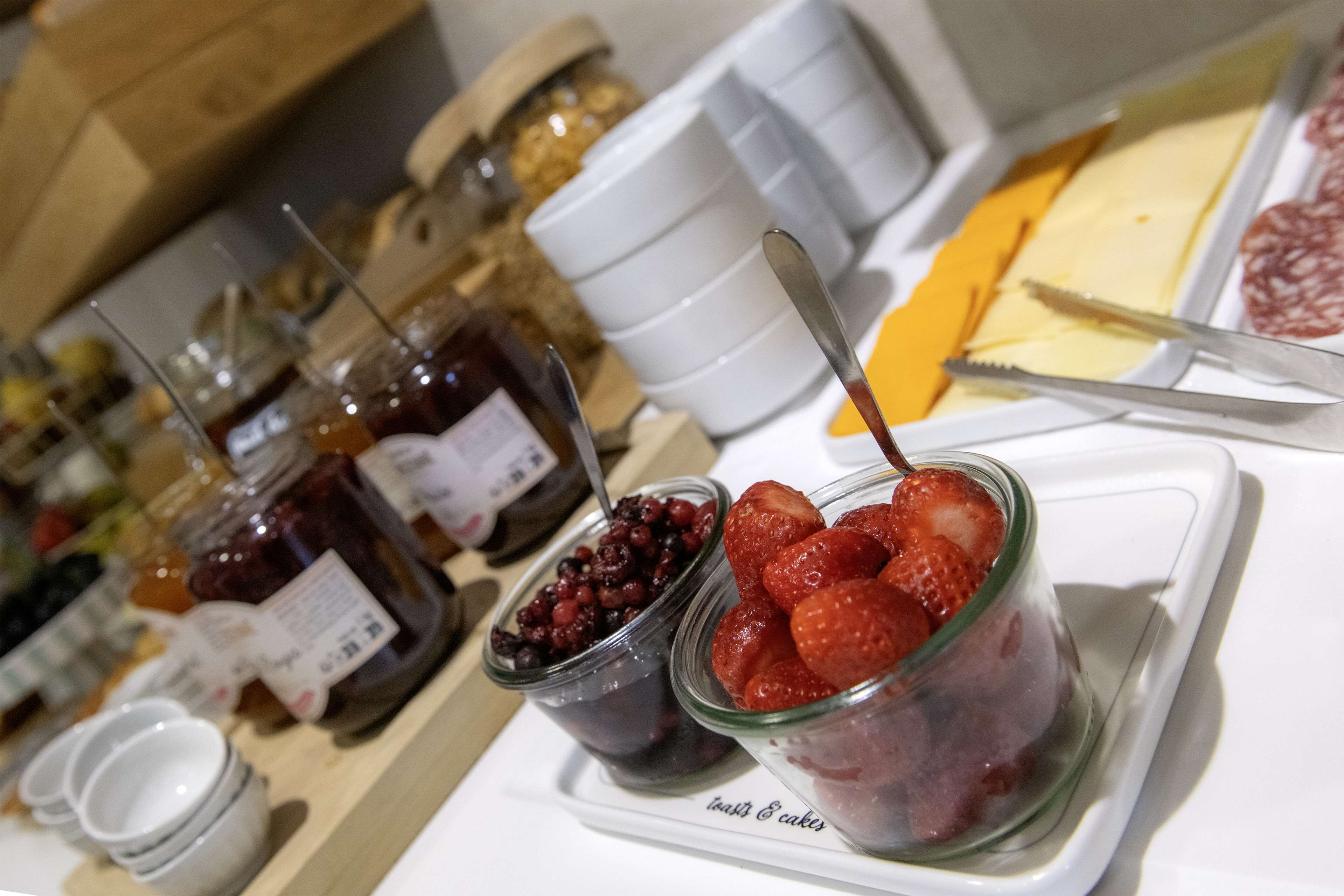 Diversos aliments, incloent pots de melmelada, maduixes i formatge, damunt d'un plat.