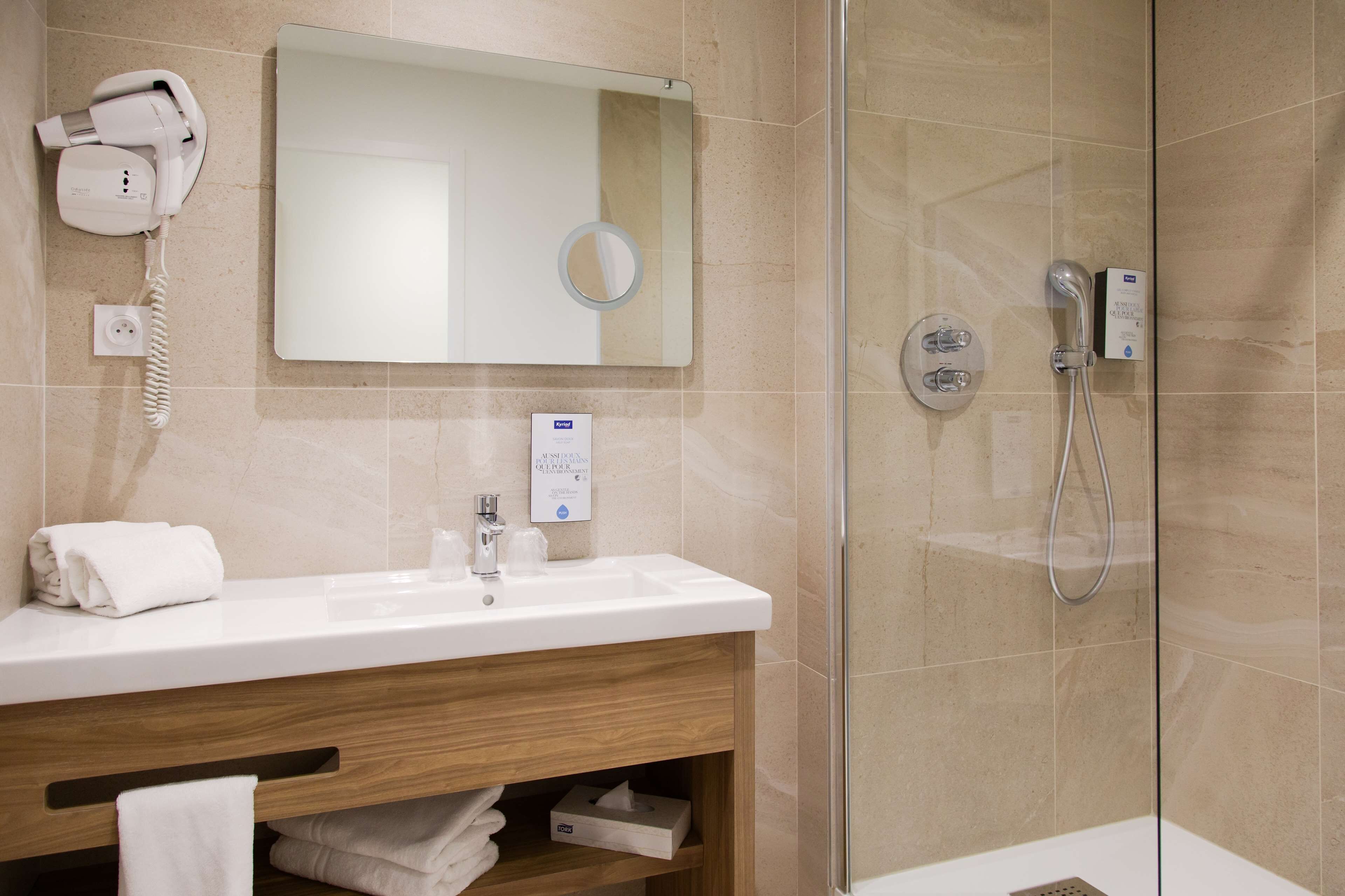 A modern bathroom with a glass-enclosed shower, a white sink, a hairdryer, and a mirror.