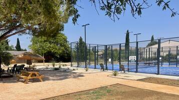 Ein Tennisplatz mit Netz, umzäunt und mit einem Picknicktisch in der Nähe.