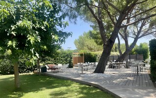 Un patio al aire libre con mesas y sillas blancas, rodeado de árboles y follaje.