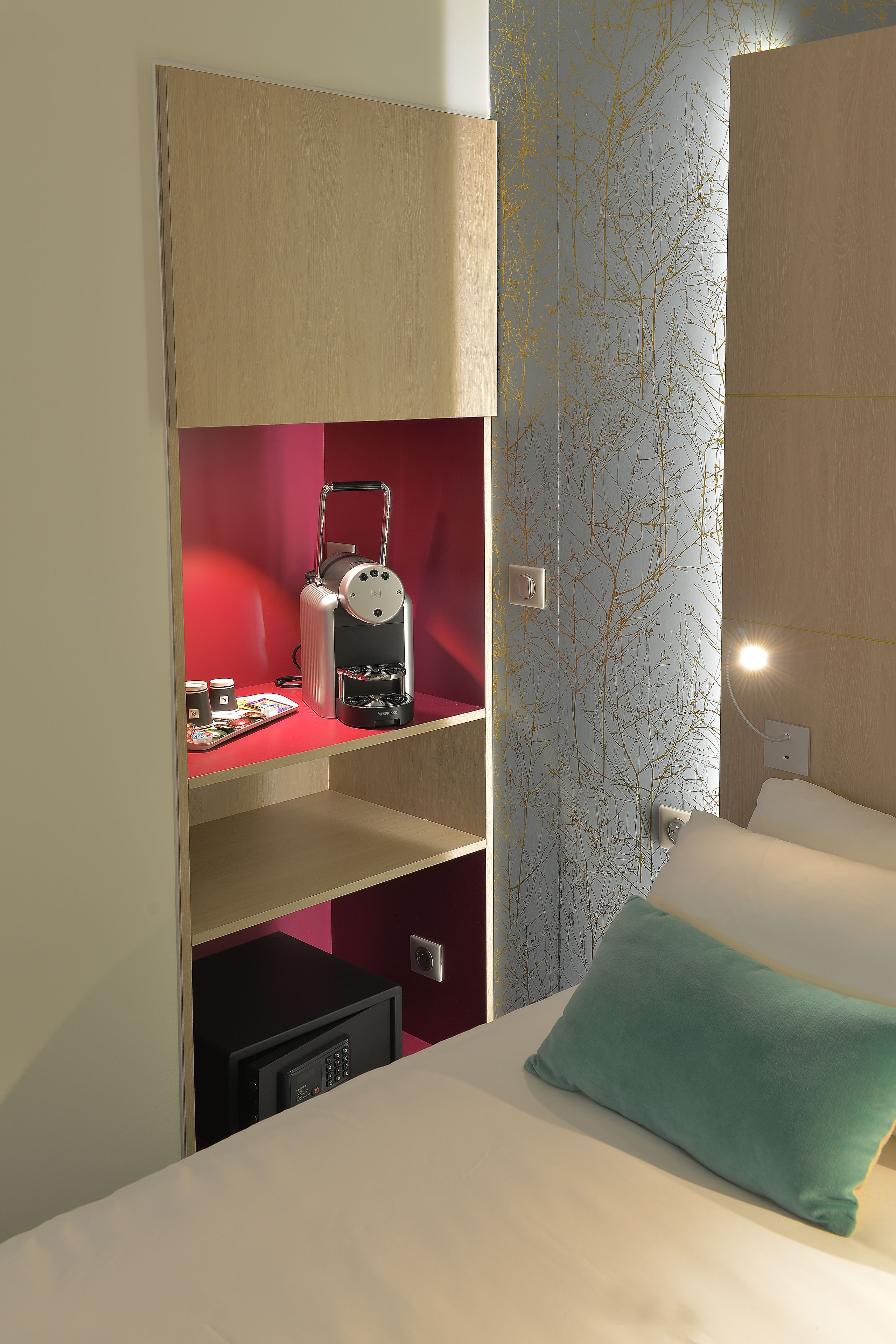A hotel room with a bed, a microwave, a coffee maker, and a red shelf.