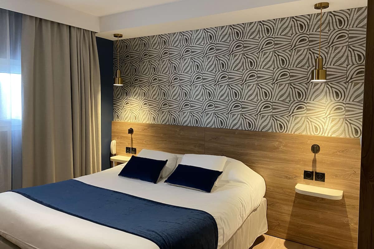Ein modernes Hotelzimmer mit einem großen Bett, zwei Nachttischen, einer Wand mit Muster und einem Fenster mit Vorhängen.