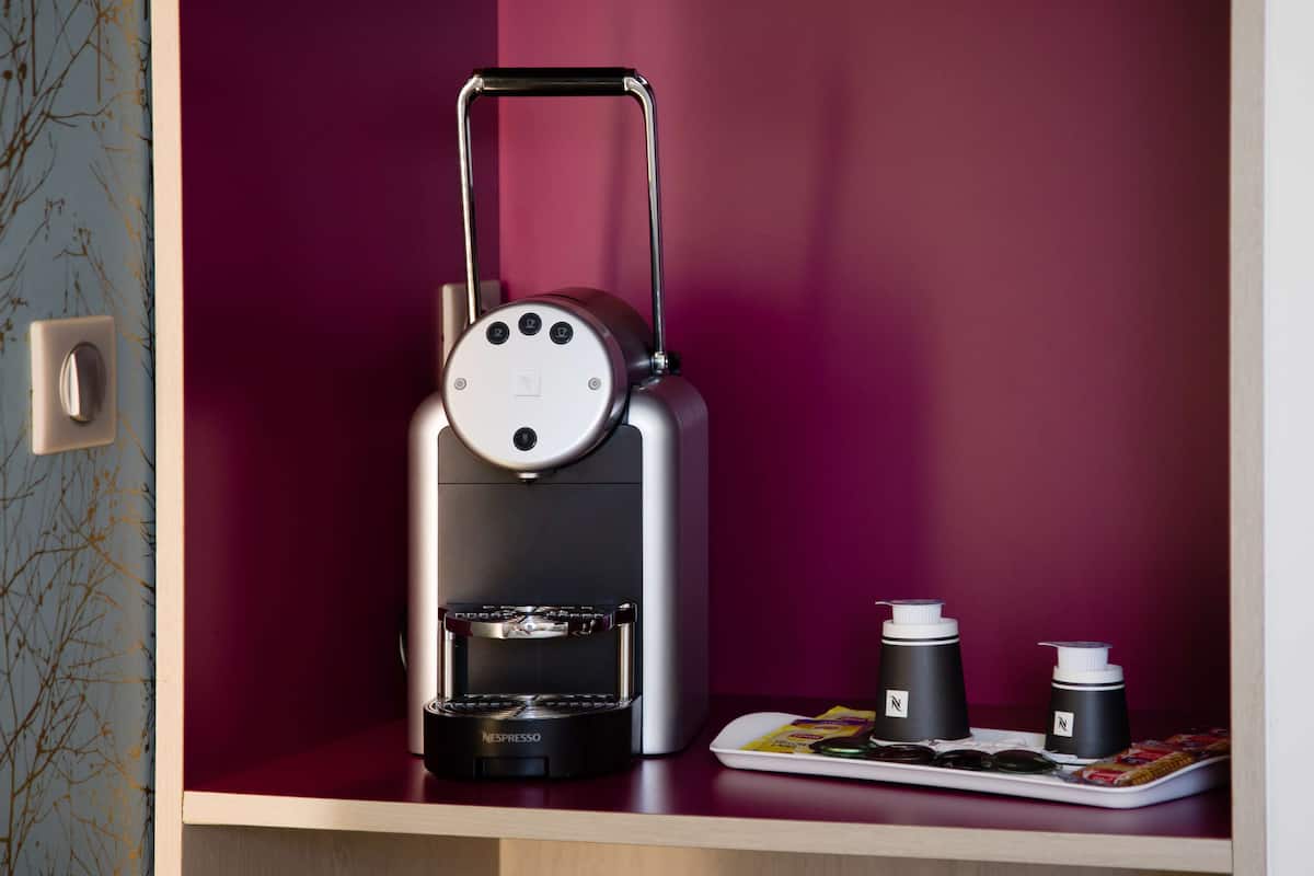 Eine Nespresso-Kaffeemaschine mit ausziehbarer Brühstange, eine Ablage für Kaffeekapseln und zwei Nespresso-Kapseln auf einer Holzoberfläche.