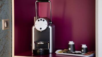 Una máquina de café Nespresso con un asa extraíble, una bandeja con cápsulas de café y dos cápsulas Nespresso sobre una superficie de madera.