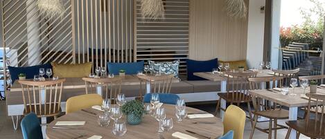 A modern dining area with round wooden tables, blue and yellow chairs, and woven ceiling lights.