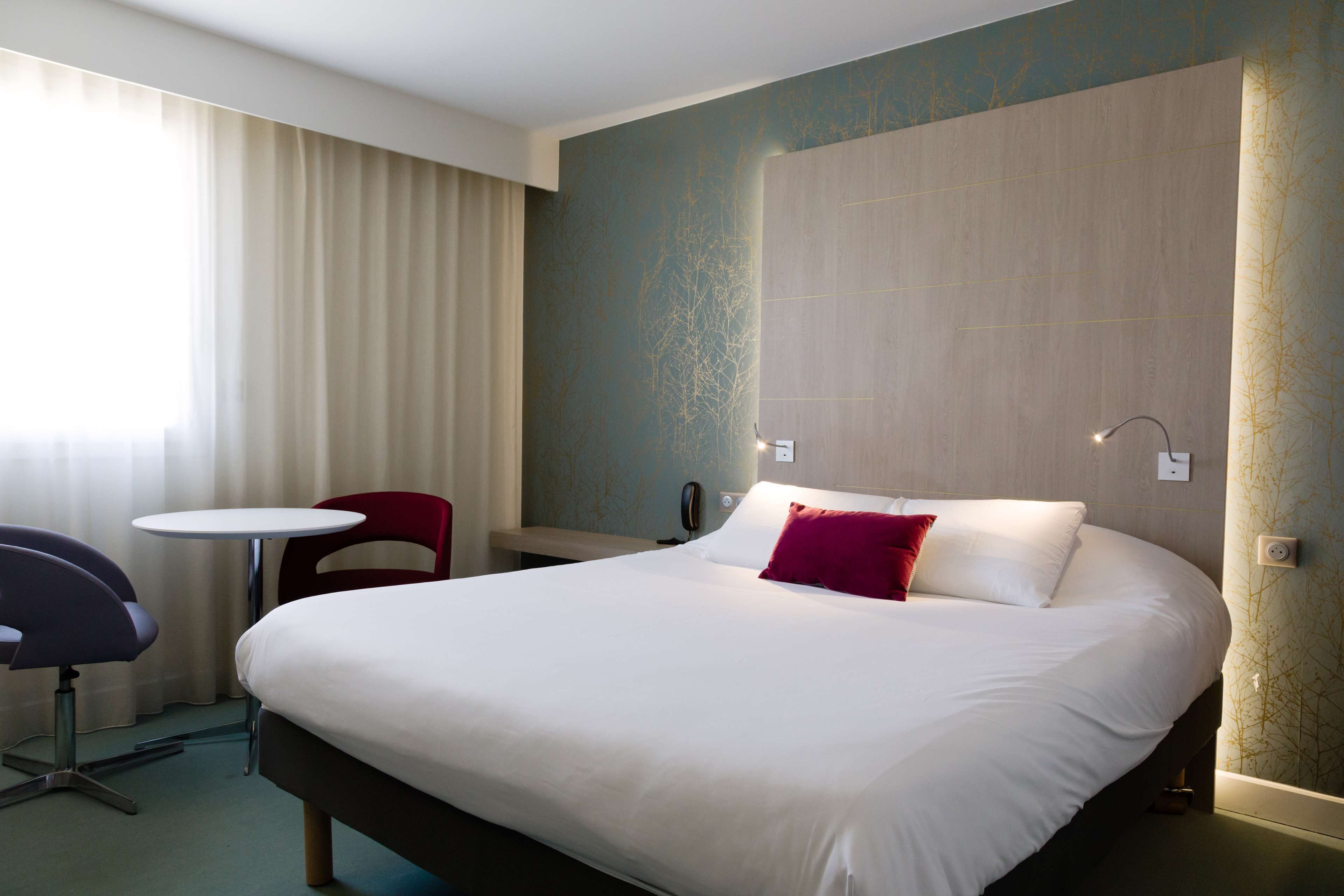 A hotel room with a large bed, a desk, a chair, and a small table.