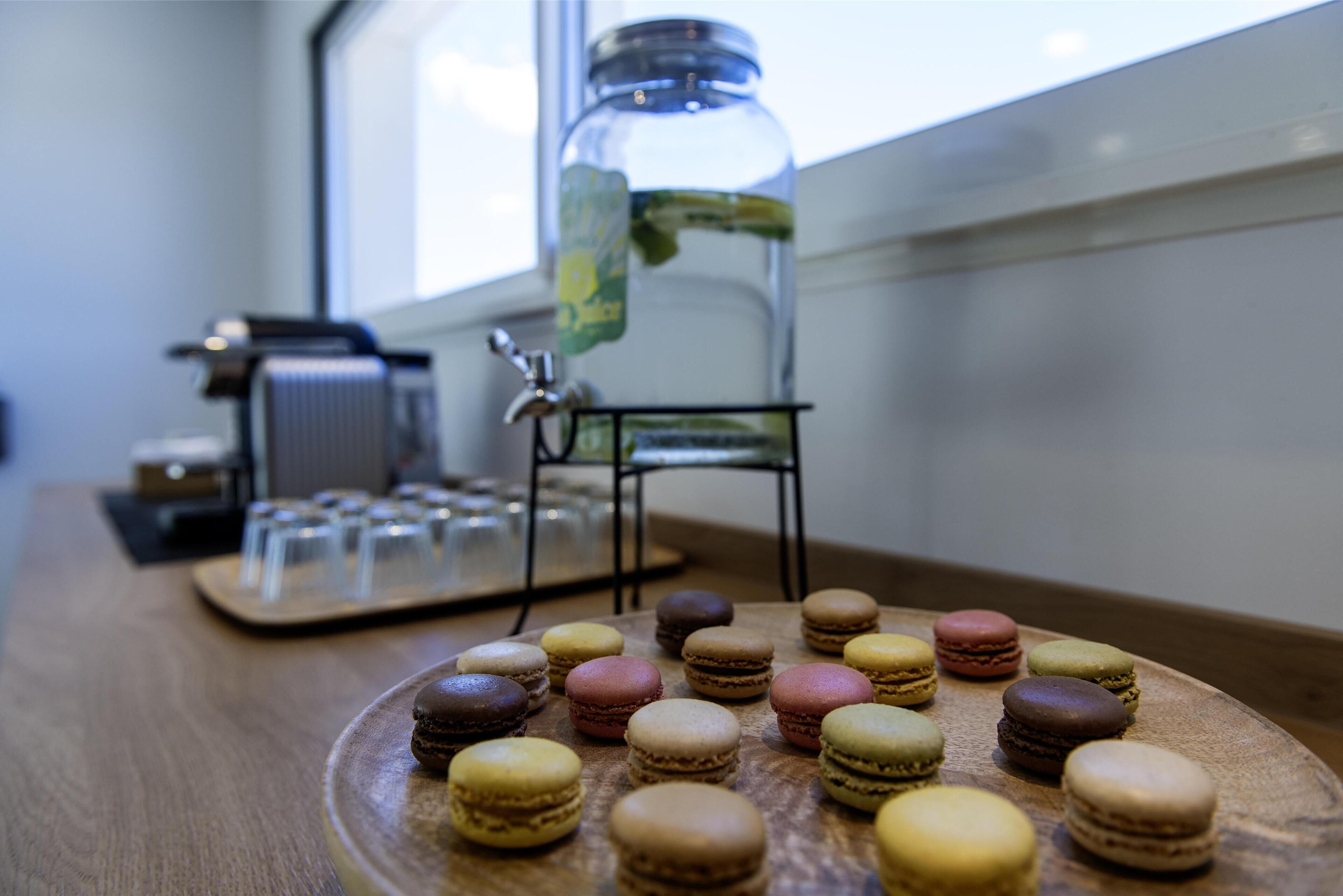 Ein Holztisch mit verschiedenen Macarons und einem Glasgefäß mit einer Grünpflanze.