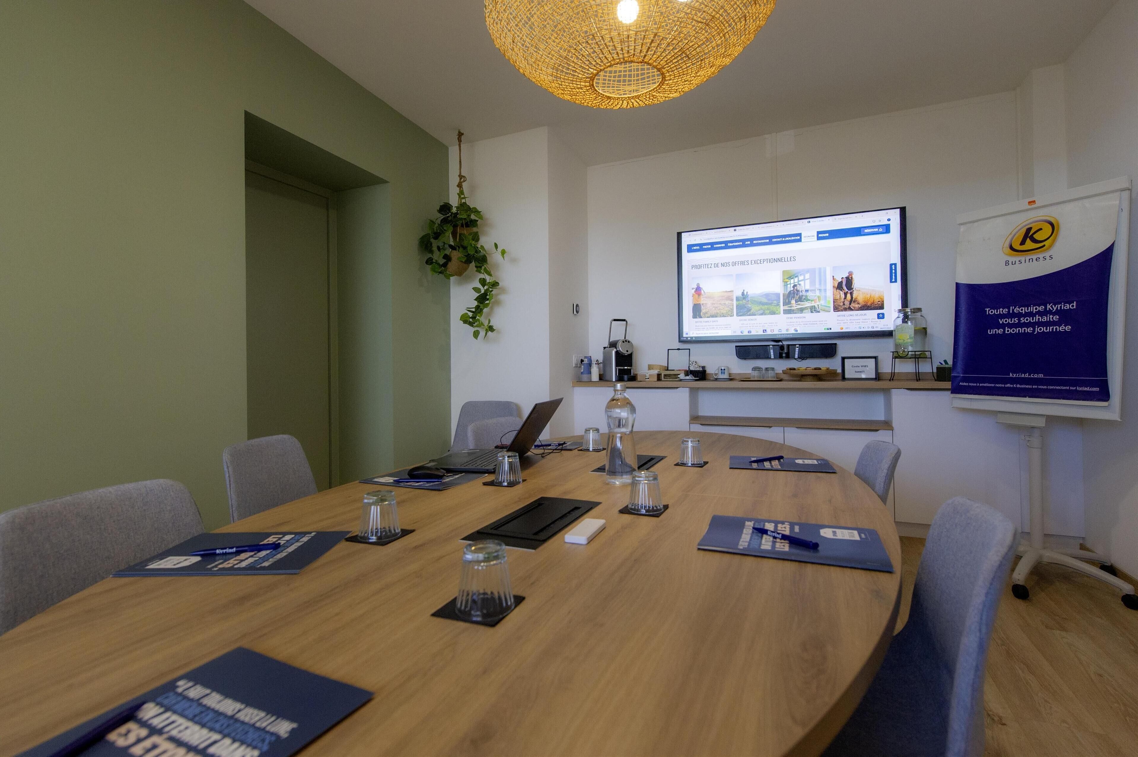 A conference room with a round table, chairs, a laptop, a projector screen, and a banner.