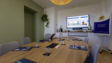 A conference room with a round table, chairs, a laptop, a projector screen, and a banner.