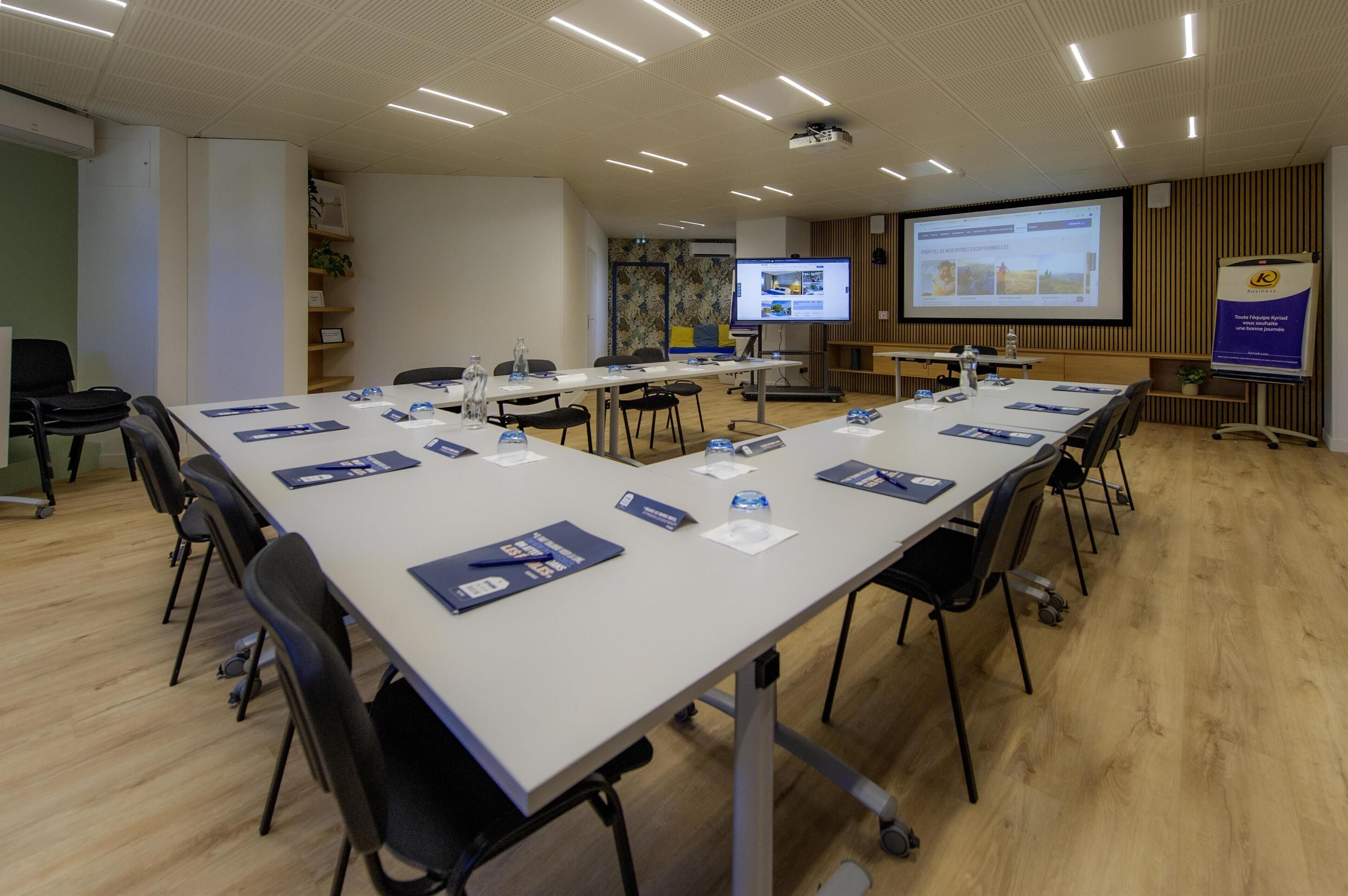 A conference room with a long table, chairs, a projector screen, and presentation materials.