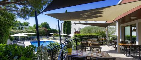 A terrace with outdoor seating, a pool, and a view of a building in the background.
