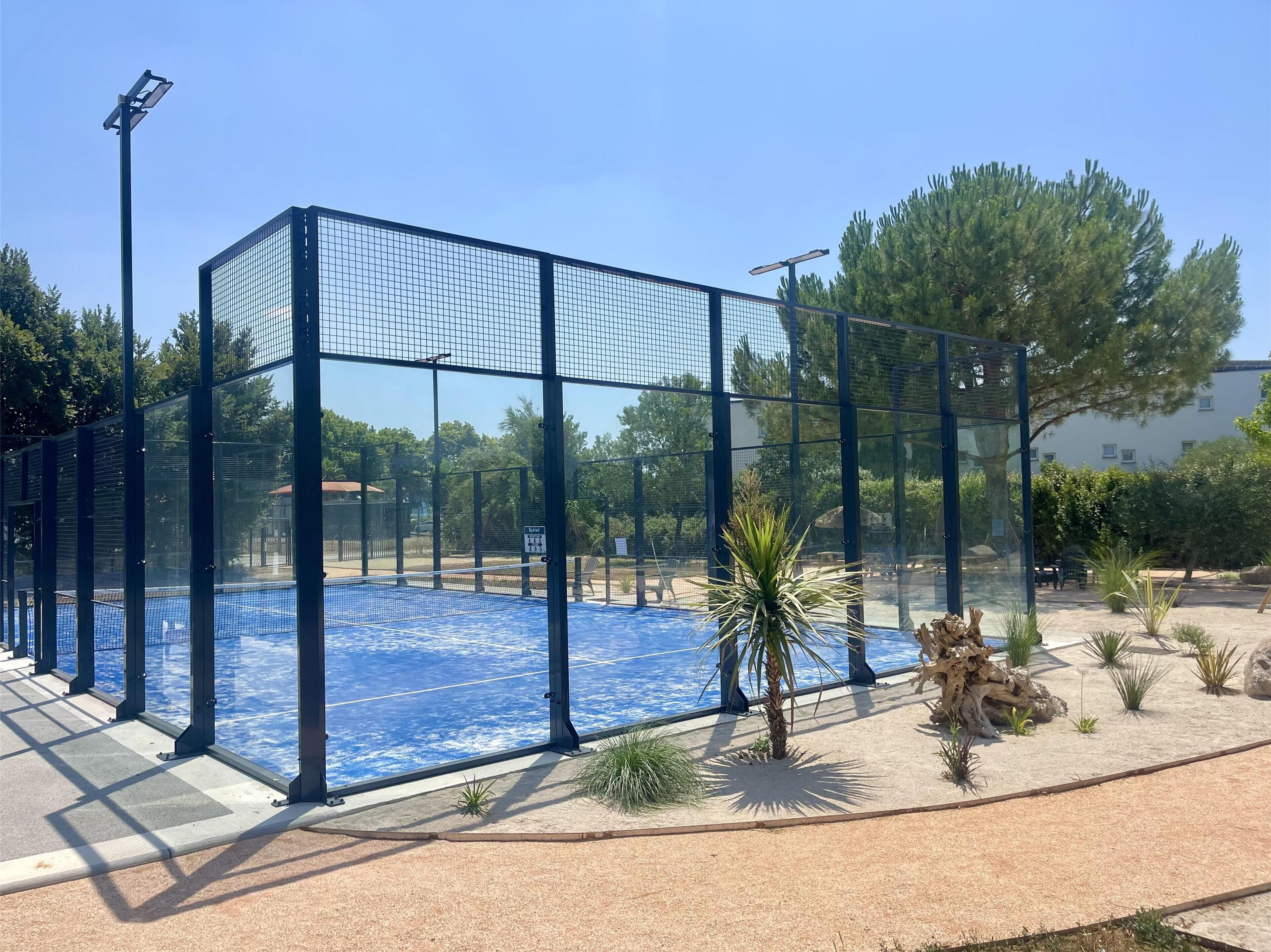 Una piscina rodeada por una valla, palmeras y un cielo azul despejado.