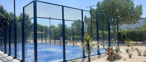 Una piscina rodeada por una valla, palmeras y un cielo azul despejado.