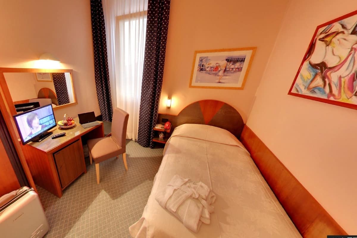Hotellihuone, jossa on sänky, työpöytä tietokoneella, tuoli, televisio ja ikkuna, jossa on verhot.