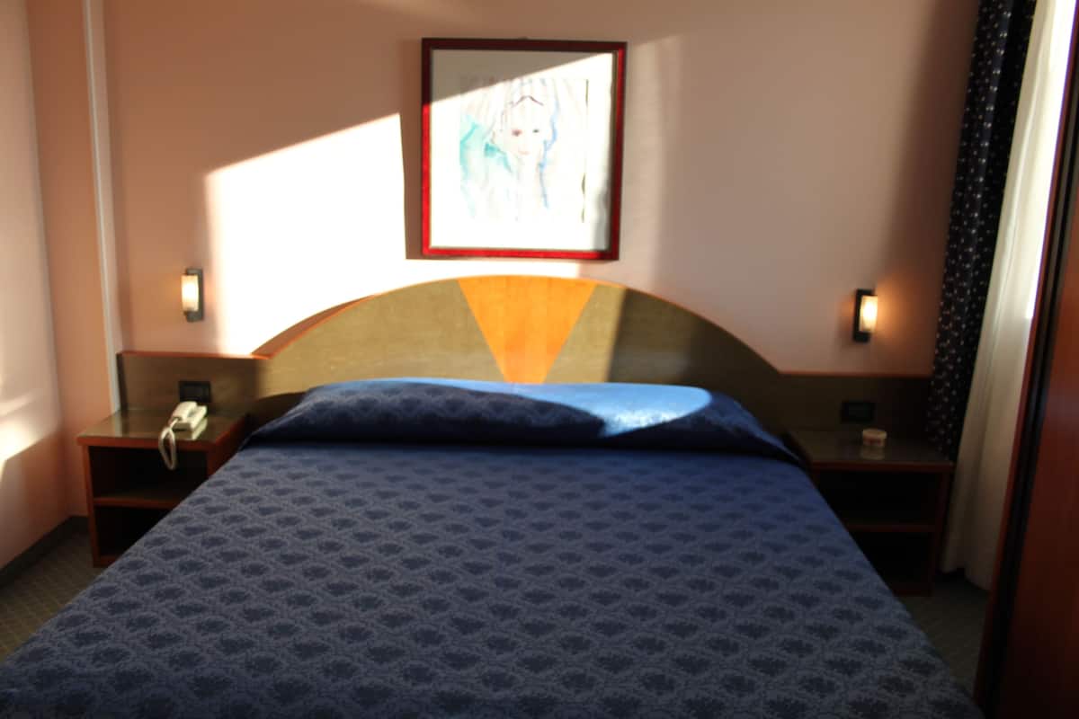 Hotellihuone, jossa on sänky, kaksi yöpöytää, seinälle asennettu puhelin ja sängyn yläpuolella oleva kehystetty kuva.