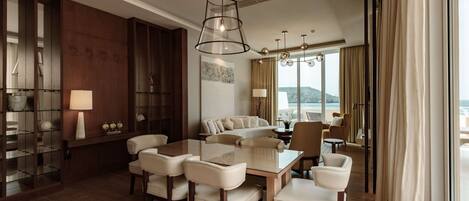 A spacious room with a dining area, a sofa set, and a large window offering a view of the sea.
