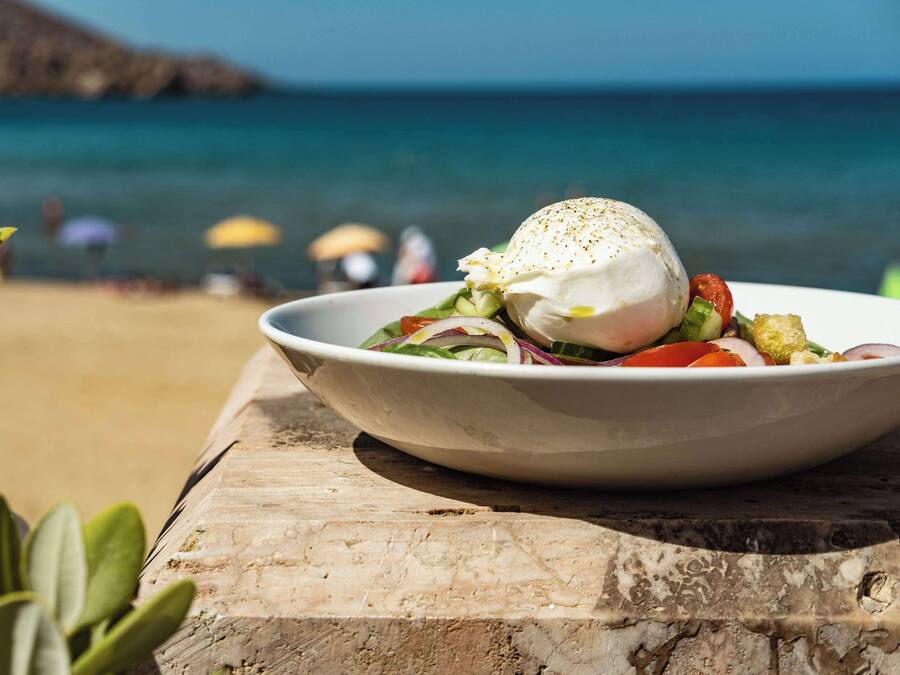 Eine Salatschüssel mit pochiertem Ei auf einem Holztisch am Strand.