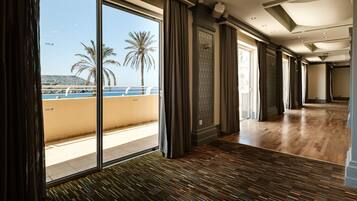 Un corridoio d'hotel con ampie finestre, pavimento in legno e vista sul mare e sulle palme.