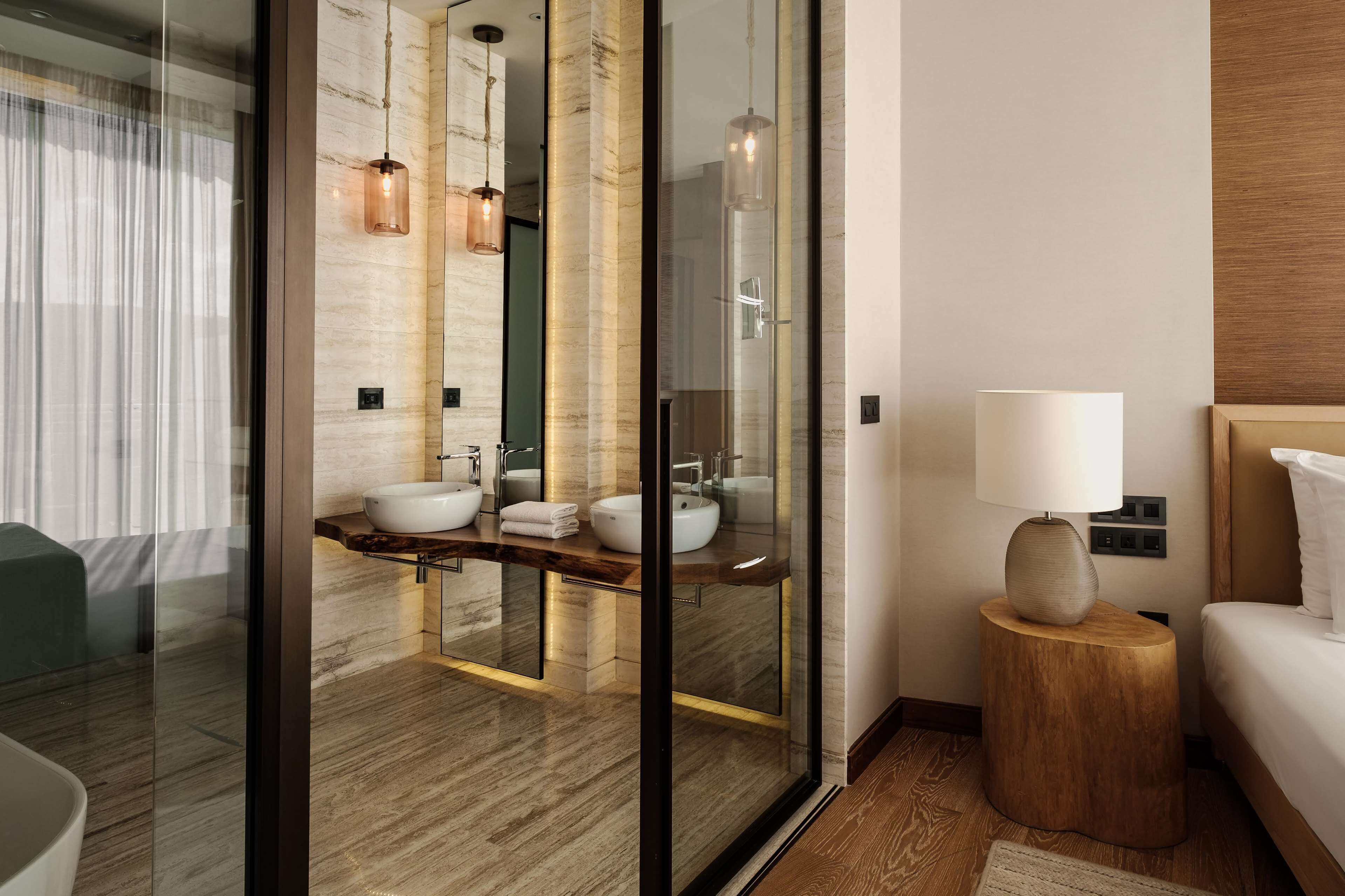 Un baño moderno con ducha envuelta en vidrio, dos lavamanos y un mueble de tocador de madera.