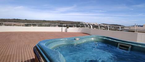 A hot tub on a wooden deck with a view of a coastal landscape.