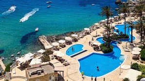 Un resort con varias piscinas, una zona de playa y barcos en el agua.