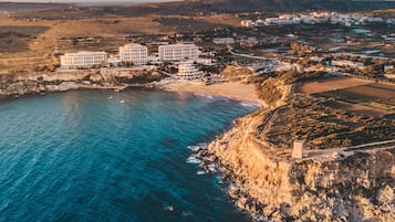 An aerial view of a coastal area with a hotel complex, rocky coastline, and surrounding landscape.